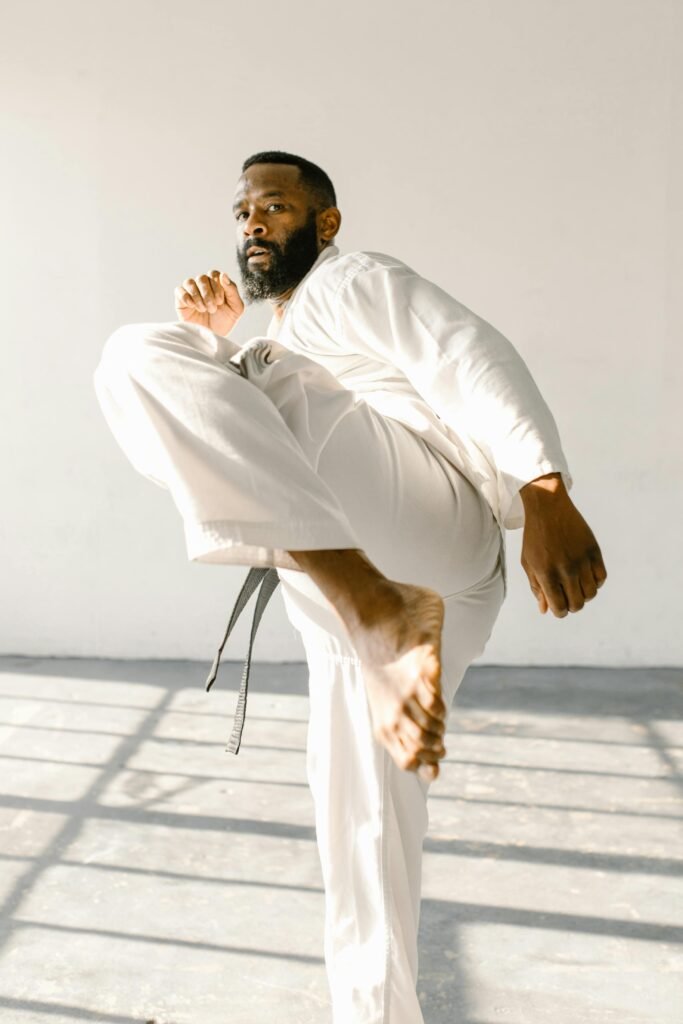Bearded martial artist practicing high kick in a sunlit studio