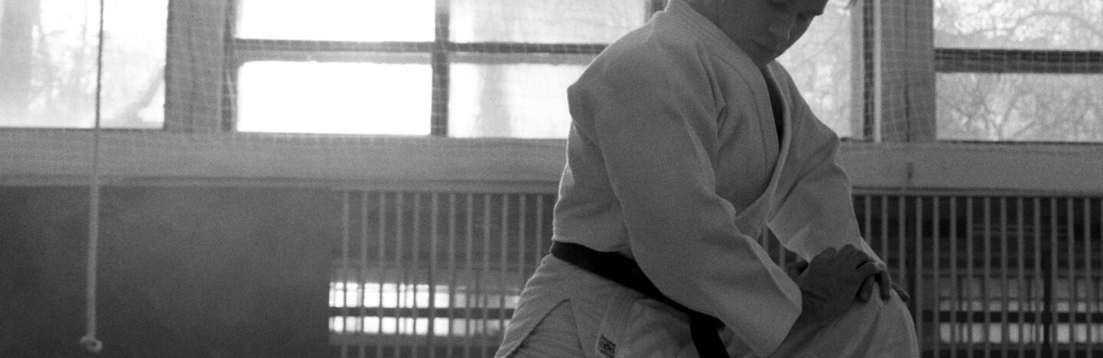 An adult practicing martial arts in a monochrome indoor setting, emphasizing focus and discipline.
